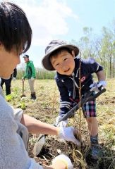 大きく育ってと願いを込めて植樹する親子連れ