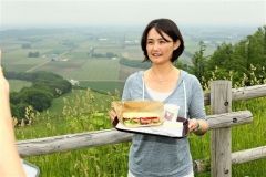 新嵐山からの景色を背景に芽室産にこだわったランチセットをPRする井澤実行委員長