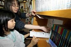 職員（奥）にヒントをもらって図書館内に隠された謎を解く子供
