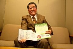 同講座の生徒手帳とパンフレットを手に笑顔を見せる金田会長