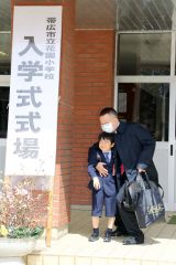 父親に抱きしめられ、玄関前で記念写真に納まる新入生（帯広花園小で、後藤貴子通信員撮影）