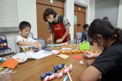 講師（右）にアドバイスをもらってヘビのおもちゃ作りに挑戦する子ども（左）