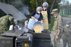 炊事車で自衛官の指導を受けながら豚汁づくりに挑戦する生徒。投入しているジャガイモは更農産