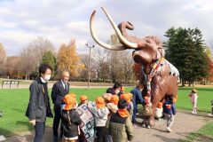 マフラーとブランケットが取り付けられたナウマンゾウの親子模型を取り囲む園児ら