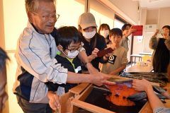 講師（左）にアドバイスをしてもらって雌のシロザケの腹部から卵を取り出す子どもら