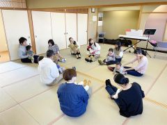 膝の上の子どもを歌に合わせて揺らす親子と松井さんら（左から４人目）（