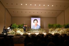 遺影が掲げられたステージで演奏するピアニストの長尾さんとバイオリニストの和光さん