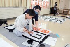 ボランティアのアドバイスを聞きながら字を書く児童