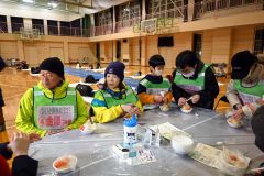 夕食として振る舞われた炊き出しの“鳥ジャガ”を食べる参加者ら（１７日午後６時４０分ごろ、下音更中体育館）