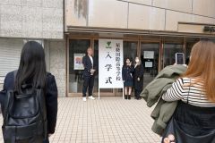 看板前で保護者と記念撮影する新入生