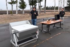 遠隔操作でカバーが開閉する機能をを説明する野口部長（中央）