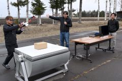 ドローンが配送した荷物を無人で受け取る装置の機能を説明する野口部長（中央）