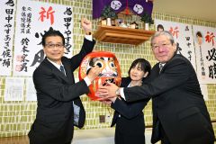 初当選を果たし、ダルマに目を入れ支持者たちに向かってガッツポーズをする田中氏（左）。中央は妻朋子さん、左は北藤利通選対本部長（２１日午後９時１０分ごろ、広尾町内の選挙事務所で。金野和彦撮影）