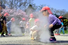 開花したサクラを背にミスト噴水で遊ぶ園児たち（２６日、午前１０時半ごろ、音更町役場前で。金野和彦撮影）