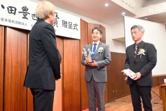 しりあがりさん（左）からトロフィーを受け取った岩井社長（中）と中村取締役