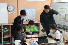 室谷さん（左）の助言を受けながら国の予算について話し合う児童たち