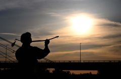 帯広カムイトウウポポ保存会による弓の舞「ク　リムセ」。弓を掲げる男性を夕日が照らす。狩人が鳥を撃とうとした時、鳥が美しく撃つことができなかったという物語からこの踊りができたと伝わる。神々への奉納の踊りとして儀式や祭事の時に踊られるほか、近年では男性の代表的な踊りとして公演などで披露されている