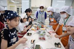 調理した食材を容器に詰めて弁当を仕上げる児童ら（左から４人目が講師の梅本さん）