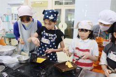 講師の梅本さん（左）と帯広大谷短大の学生（右）にサポートしてもらって玉子焼きを調理する児童ら