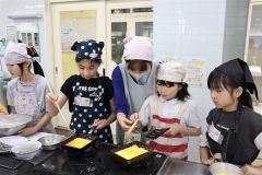 講師の梅本さん（左から３人目）にアドバイスしてもらいながら玉子焼きを調理する児童ら