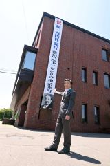 役場庁舎に掲げられた懸垂幕を前にする阿部町長（７日午前１１時５５分ごろ）