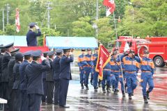 森田村長（壇上）や消防署幹部らの前を行進する団員
