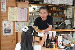 「北の屋台」の各店舗に啓発ラベル付き日本酒瓶を手渡す阪口百合乃さん（左）（１０日午後５時２０分ごろ、北の屋台）