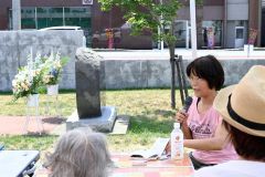 帯広空襲の碑の横で高橋キソさんの証言を語る浅見さん