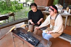 自然の中、たき火でパンとチーズを焼いて楽しむ来場者（２０日午前１０時５５分ごろ）