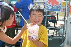 「猛暑日」となった帯広で汗をかきながらありついたかき氷に笑顔を見せる子ども（２１日午後１時２０分ごろ、帯広市街地で開催された帯広市まちなか歩行者天国で）