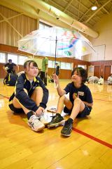 完成した傘を掲げる児童と一緒に笠に入る幕別清陵高校の生徒