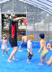年少から年長が遊ぶプールでは保育士からジョーロで水をかけてもらい遊ぶ子どもたち