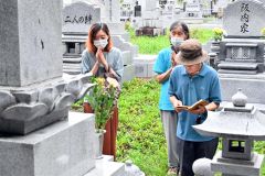 墓前でお経を唱え手を合わせる参拝者(13日午前9時50分ごろ、帯広市内の緑ケ丘墓地で)