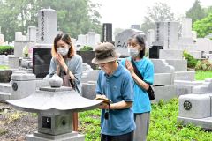 墓前でお経を唱え手を合わせる参拝者(13日午前9時50分ごろ、帯広市内の緑ケ丘墓地で)