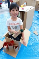 完成したお風呂に入り、セロハンで水を表現したシャワーを握る子ども