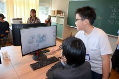 iPadで取り込んだデザインのデータを講師らに手伝ってもらって3Dプリンターにインプットする児童ら