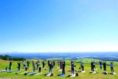 青空の下、ナイタイテラス横の芝生でヨガをする参加者