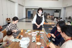 講師の飯島さん(右から3人目)のアドバイスで籠作りに挑戦する母親ら