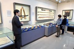 大和田さん(左)の解説を聞きながら展示資料を見る内覧会参加者