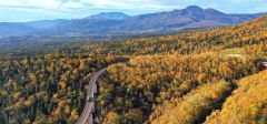 山腹一面が紅葉に包まれた上士幌町の三国峠。右奥は東大雪のニペソツ山(3日午前6時40分ごろ、塩原真がドローンで撮影)