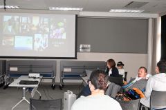 車いすに乗る当事者の山田さんと、来場者を前に原稿を読む妻の五月さん