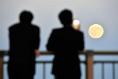 昇った満月を見入る高校生(17日午後4時40分ごろ、帯広の森の「もりの山」で。塩原真撮影)