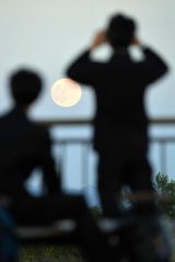 昇った満月を見入る高校生(17日午後4時40分ごろ、帯広の森の「もりの山」で。塩原真撮影)