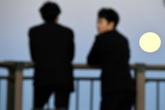 昇った満月を見入る高校生(17日午後4時40分ごろ、帯広の森の「もりの山」で。塩原真撮影)